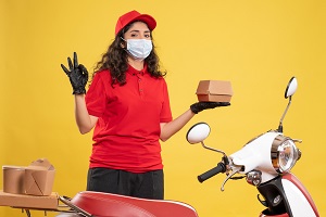 Front view female courier red uniform holding little food package yellow background delivery covid service uniform worker pandemic